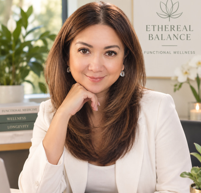 Alma, a Registered Nurse and Certified Functional Health & Medicine Coach, smiling with her hand resting on her chin in her office, beside a wall sign reading Ethereal Balance Functional Wellness